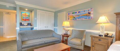 A hotel room with a striped sofa, a patterned armchair, a wooden nightstand, and a bed.
