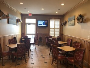 Un restaurante con paneles de madera, varias mesas y sillas, un televisor mostrando un mapa y una ventana con persianas.