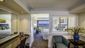 A hotel room with a bed, a chair, a table with a vase, a window with blinds, and a view of the ocean.