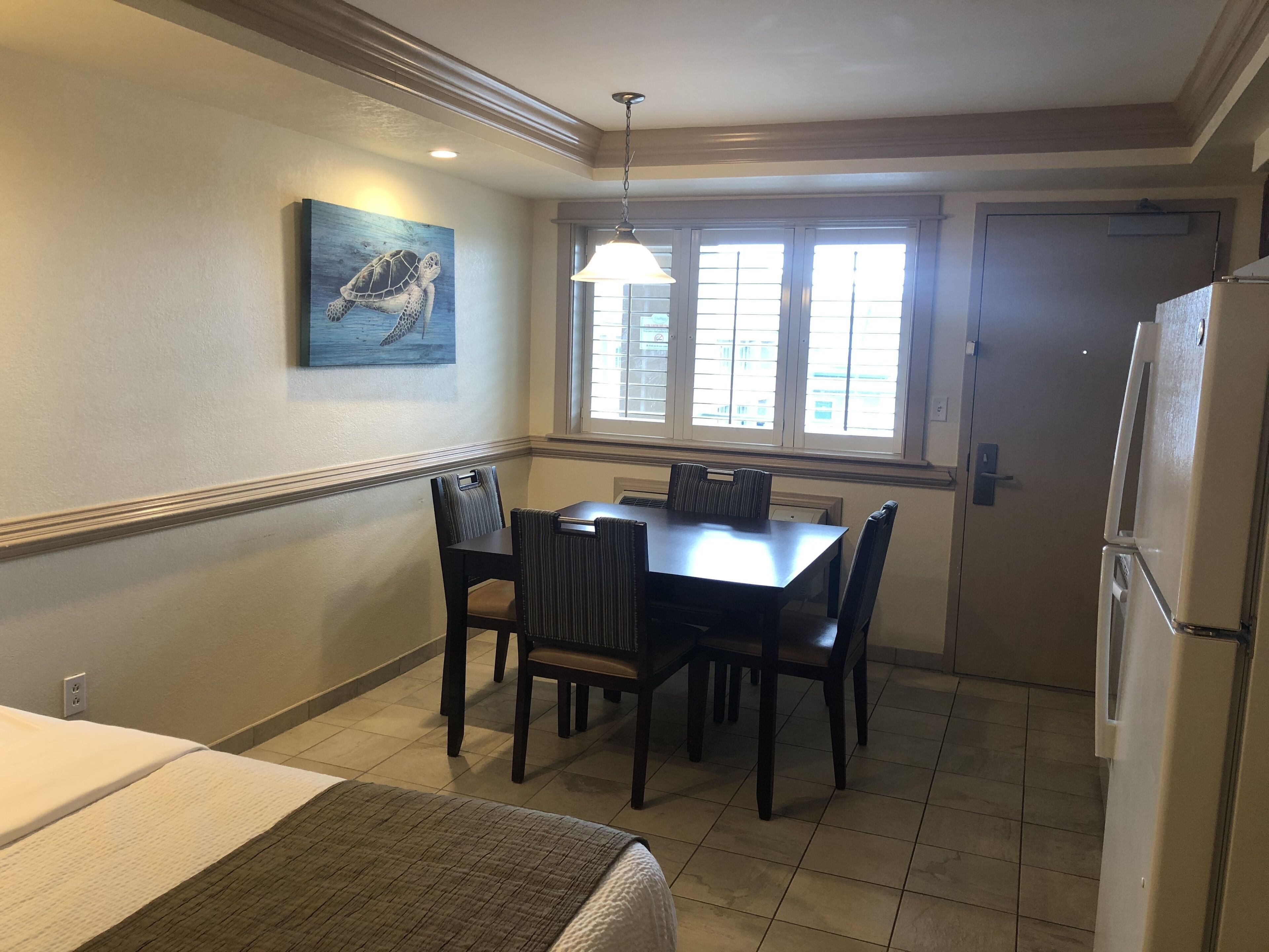 A compact kitchen with a dining table, chairs, a refrigerator, and a window with blinds.