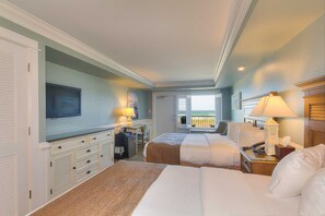 Habitación de hotel con dos camas, un escritorio, televisión y un balcón con vistas.
