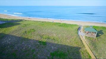 An aerial view of a beach with a small wooden structure, a grassy area, and the ocean in the background.