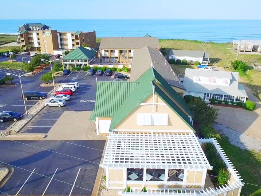 Vista aérea de un hotel costero con estacionamiento, vistas a la playa y un pequeño pabellón.