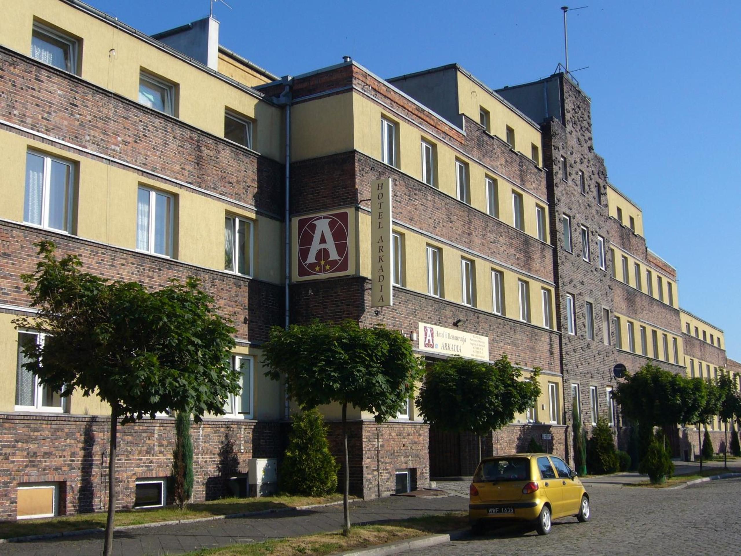 Ett hotell med flera våningar, ett framträdande logotyp i form av bokstaven ”A”, en fasad av tegel och en färgskala i gult och brunt.