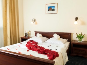 A hotel room with a bed, a nightstand, a bedside table with a vase of flowers, a picture on the wall, and a window with curtains.