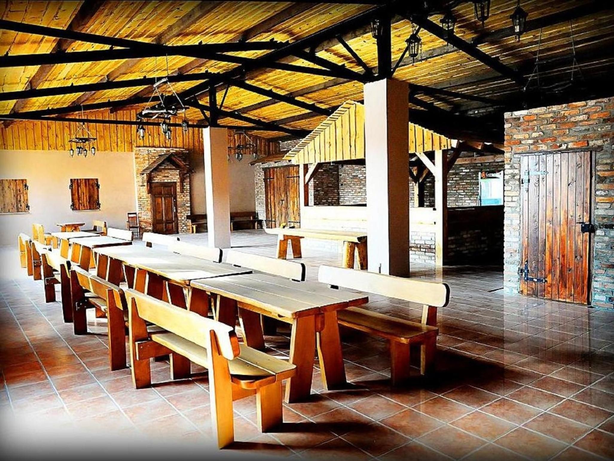 A long dining hall with wooden benches and tables, a high ceiling with exposed beams, and brick walls.