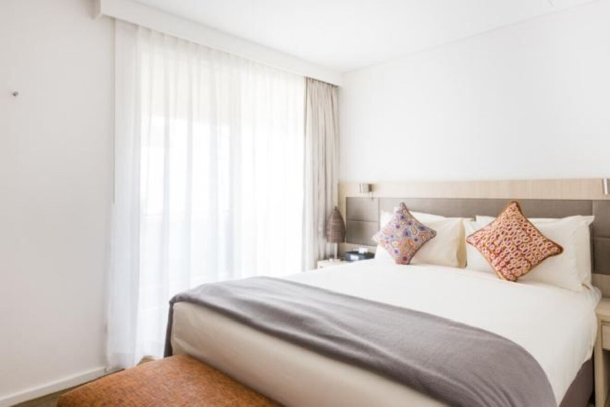 Una habitación de hotel con una cama, una mesita de noche y un banco.