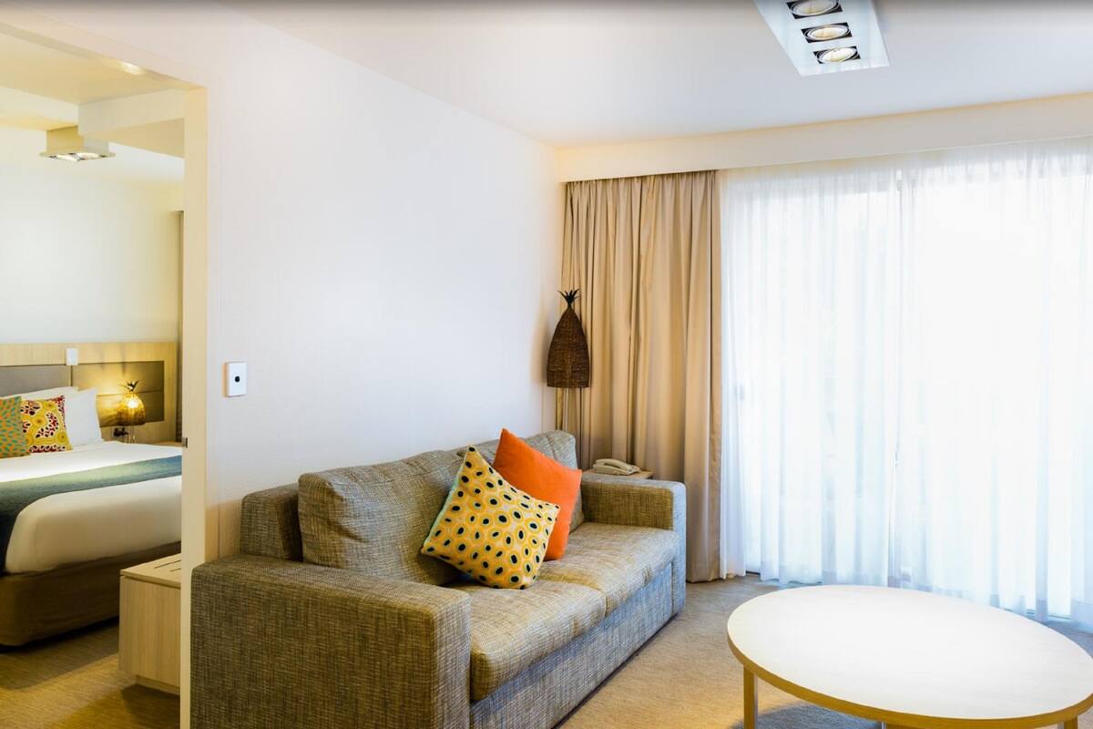 A hotel room with a bed, a sofa, a round table, and a large window with curtains.