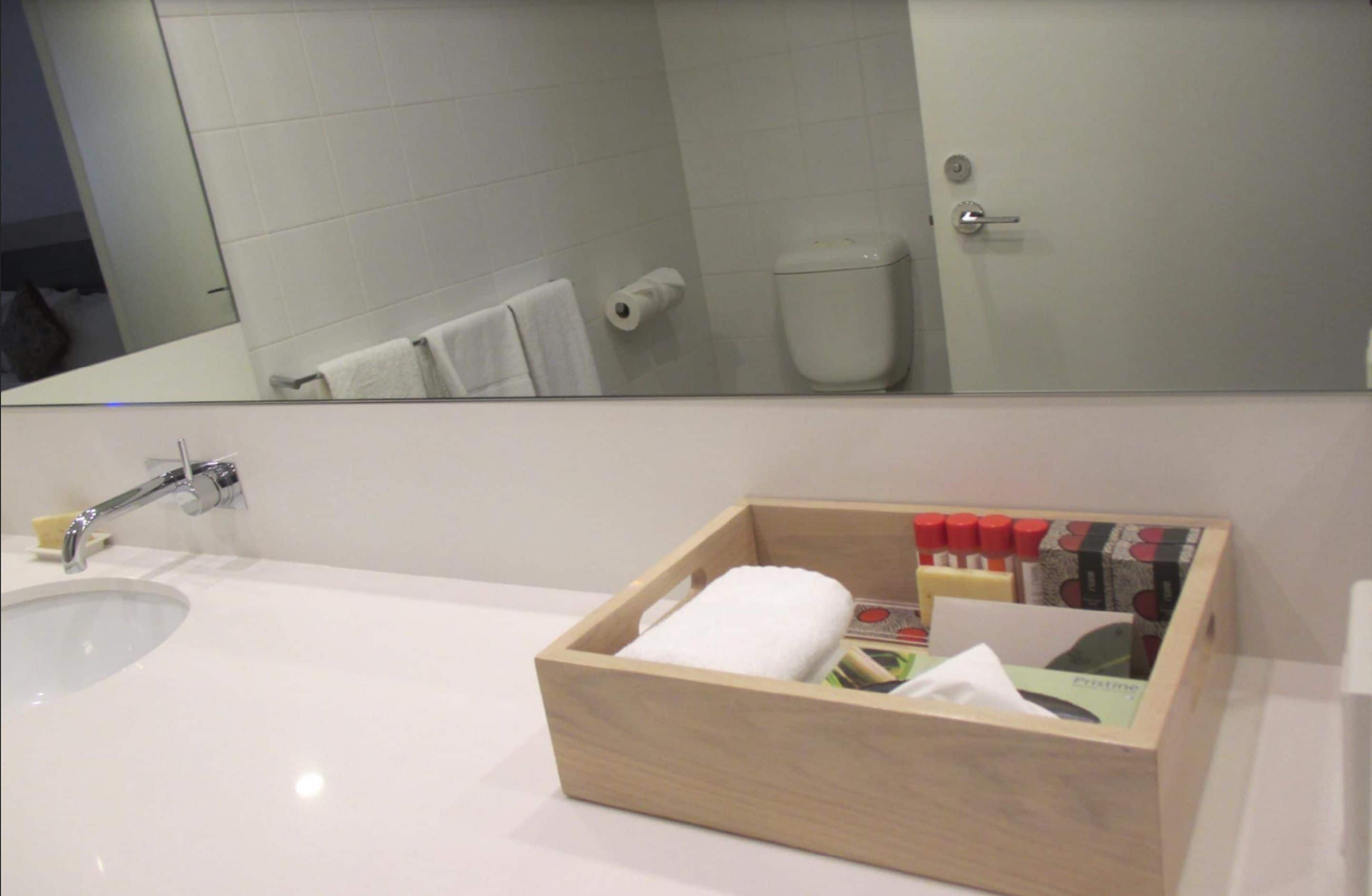 A bathroom with a white sink, a mirror, and a wooden box containing toiletries.