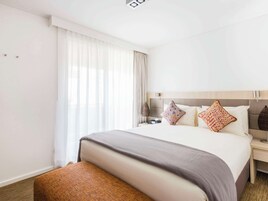 Una habitación de hotel con una cama grande, una mesita de noche, una lámpara y una ventana con cortinas.