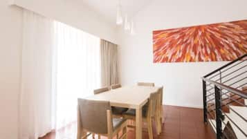 A dining area with a wooden table and chairs, a large abstract painting on the wall, and a staircase with a metal railing.
