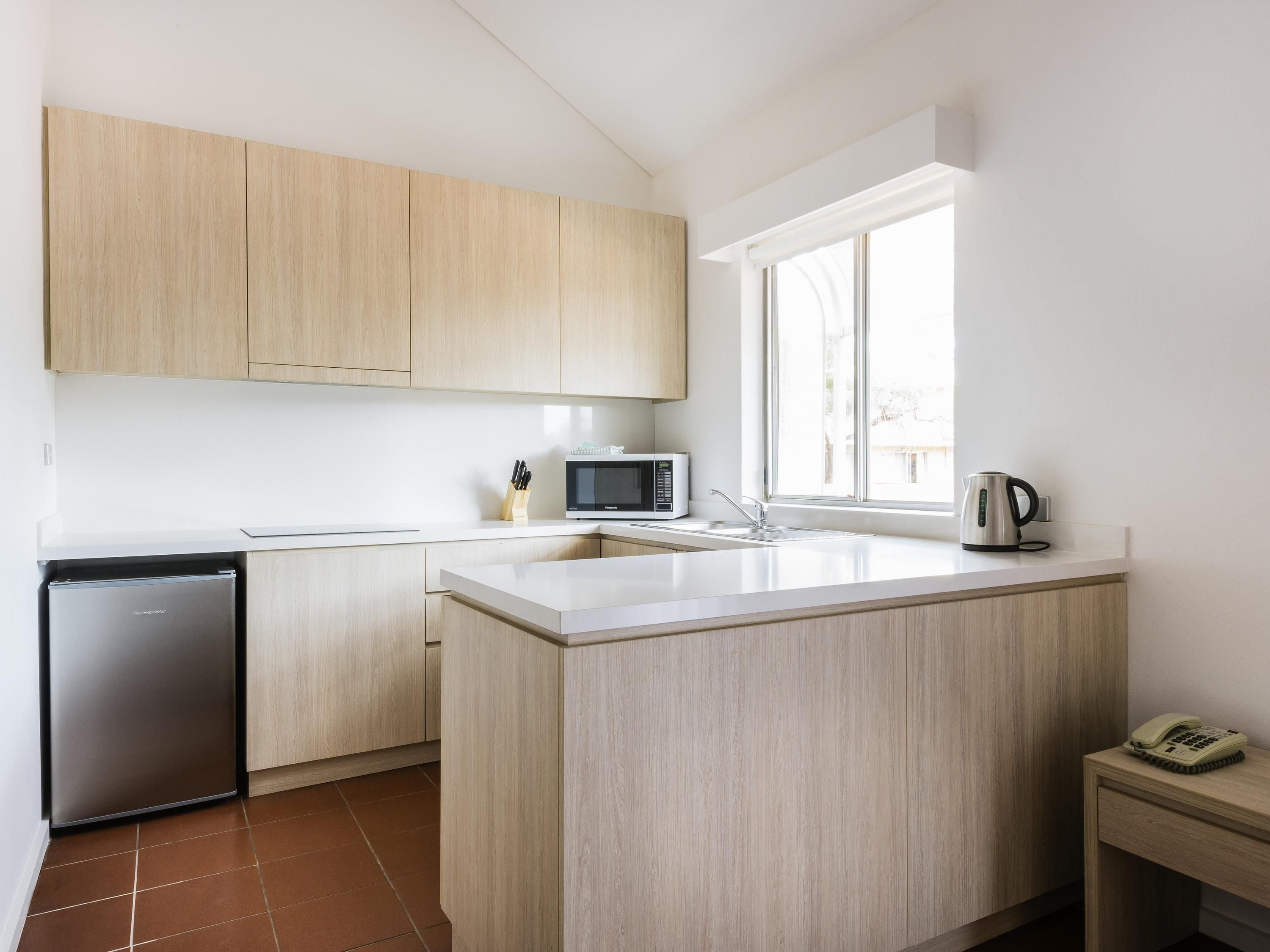Une cuisine moderne avec des meubles en bois, un four à micro-ondes encastré, une bouilloire et un petit réfrigérateur.