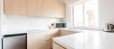 A modern kitchen with white cabinets, a built-in microwave, and a kettle on the counter.