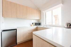Una cocina moderna con armarios blancos, un microondas integrado y un hervidor sobre la encimera.