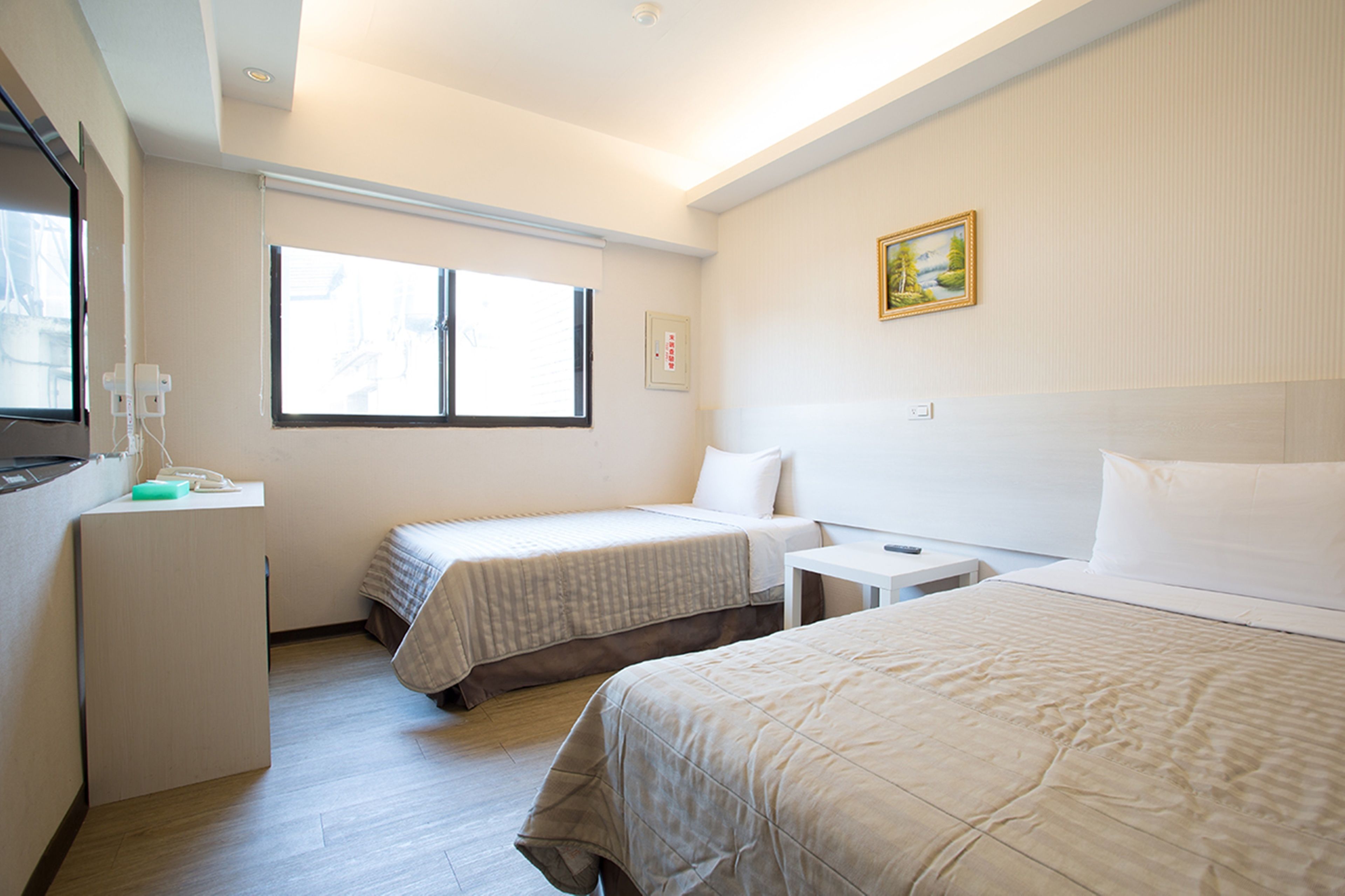 A hotel room with two single beds, a desk, a chair, a small table, and a window.