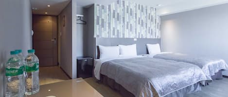 Habitación de hotel con dos camas, una mesita de noche con una taza y botellas de agua, una lámpara de pared y una puerta que da a otra habitación.