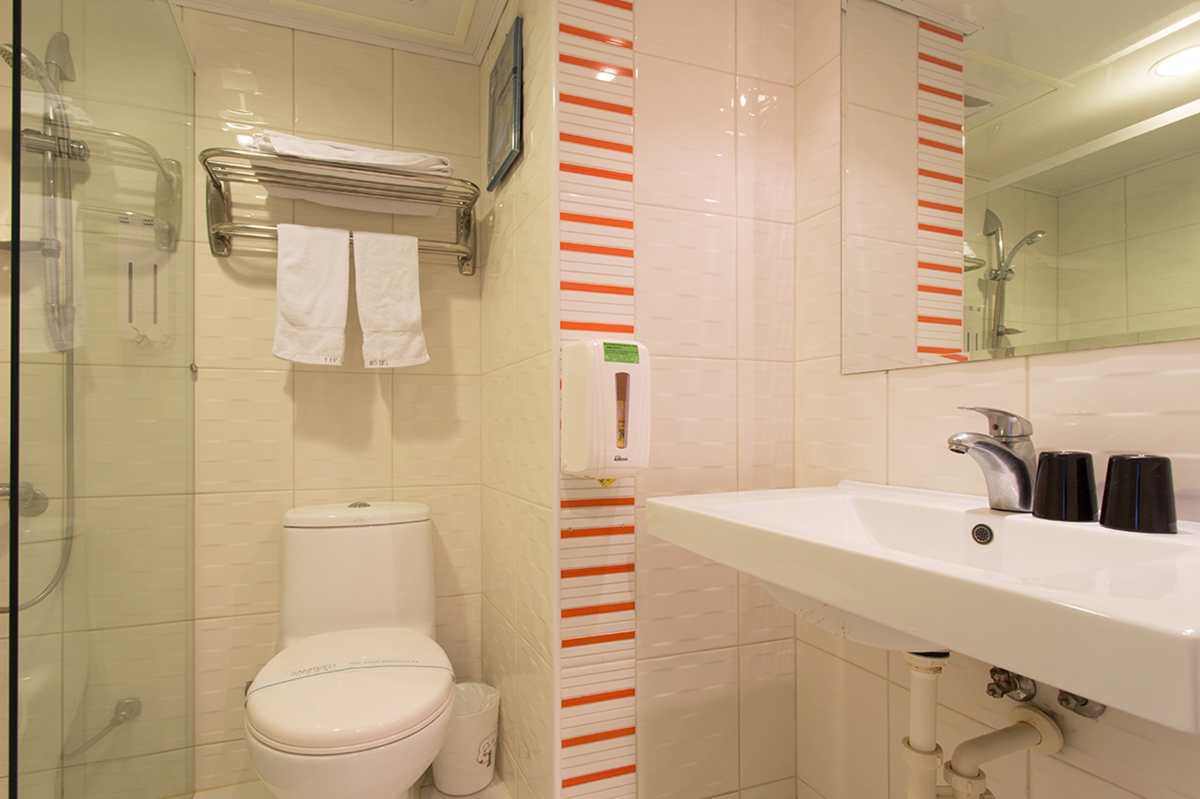 A bathroom with a toilet, a glass shower enclosure, a sink with black soap dispensers, and a mirror.