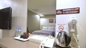 A hotel room with a bed, a desk with a telephone, a hairdryer, and a sign indicating no smoking. - Palmer Hotel (Taichung)
