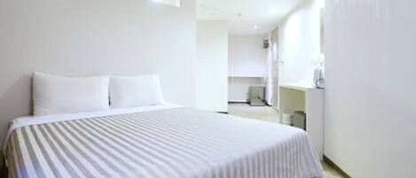 A hotel room with a large bed, a small desk, and a window.