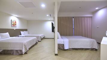 Habitación de hotel con tres camas, un ventanal con cortinas y un televisor montado en la pared.