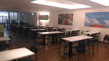 A spacious dining area with multiple tables and chairs, a large poster on the wall, and a bright ceiling light.