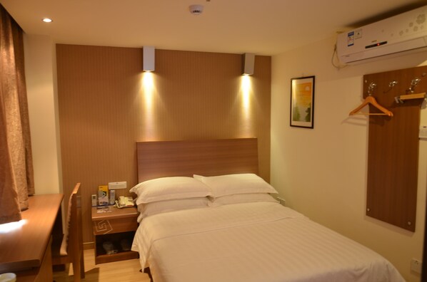 Ein Hotelzimmer mit Bett, Nachttisch und Holz-Kopfteil. An der Wand ist eine Wandklimaanlage und ein gerahmtes Bild angebracht.