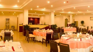 A hotel dining area with multiple round tables, chairs, and a bar counter.