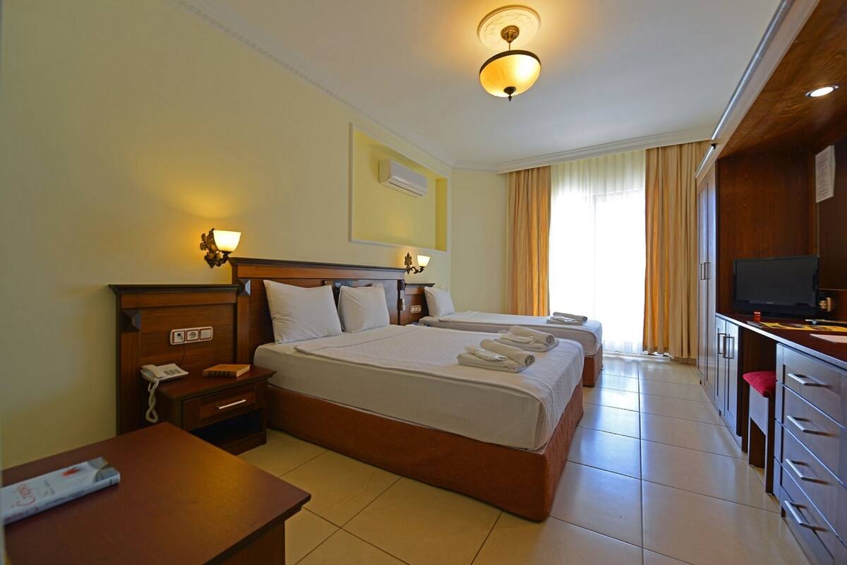 A hotel room with a large bed, bedside tables, a desk, a television, and a window with curtains.