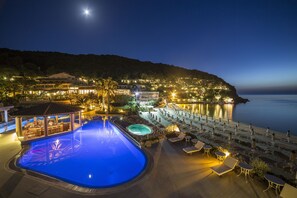 A nighttime view of a resort with a swimming pool, lounge chairs, and a beach area. - Hotel Hermitage (Portoferraio)