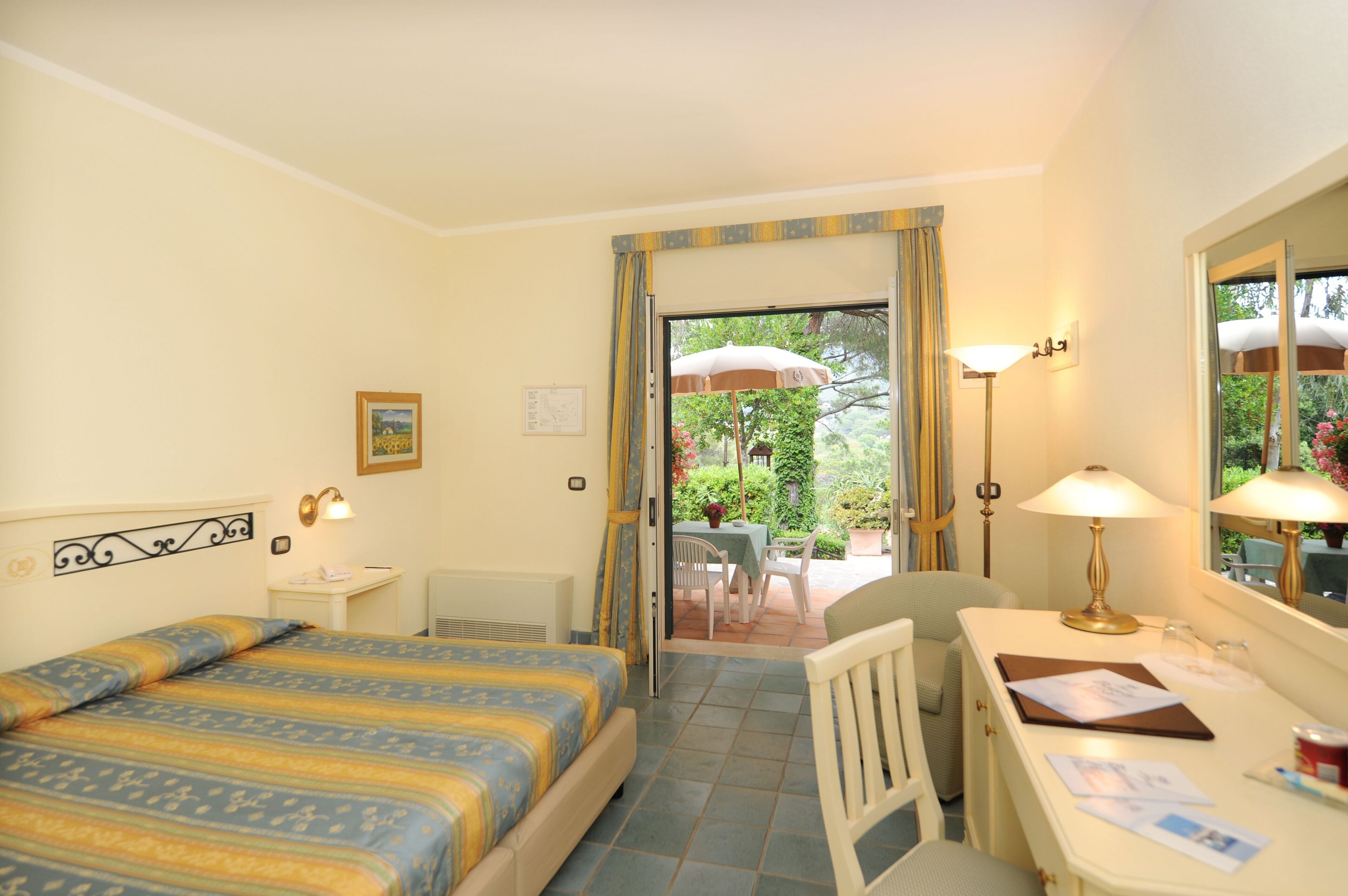 A hotel room with a bed, a desk, a chair, and a view of an outdoor patio with a table and chairs.