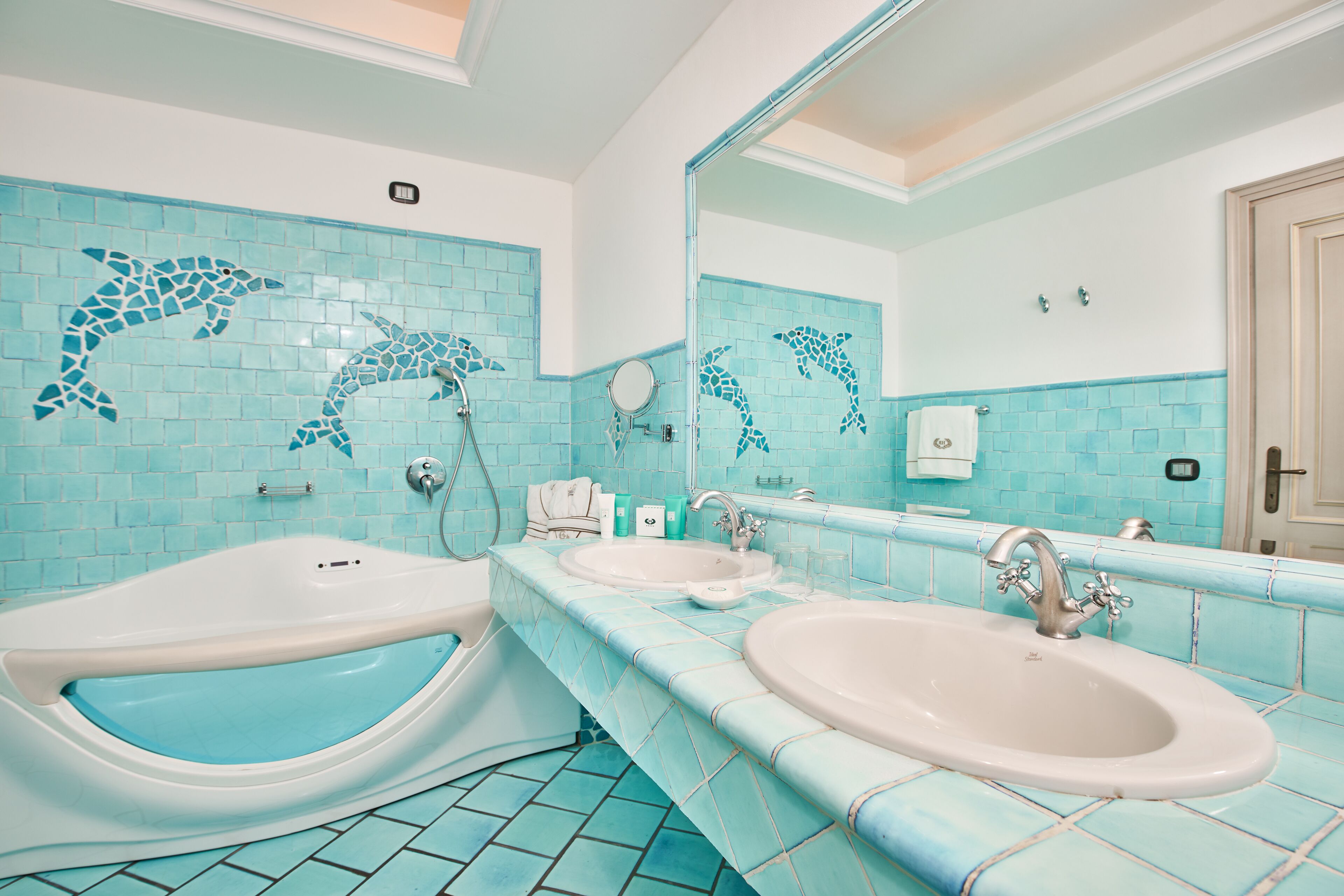 Un bagno con due lavandini, una vasca e piastrelle a mosaico con motivi di delfini.