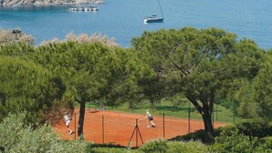Una cancha de tenis con vista al mar y barcos al fondo.