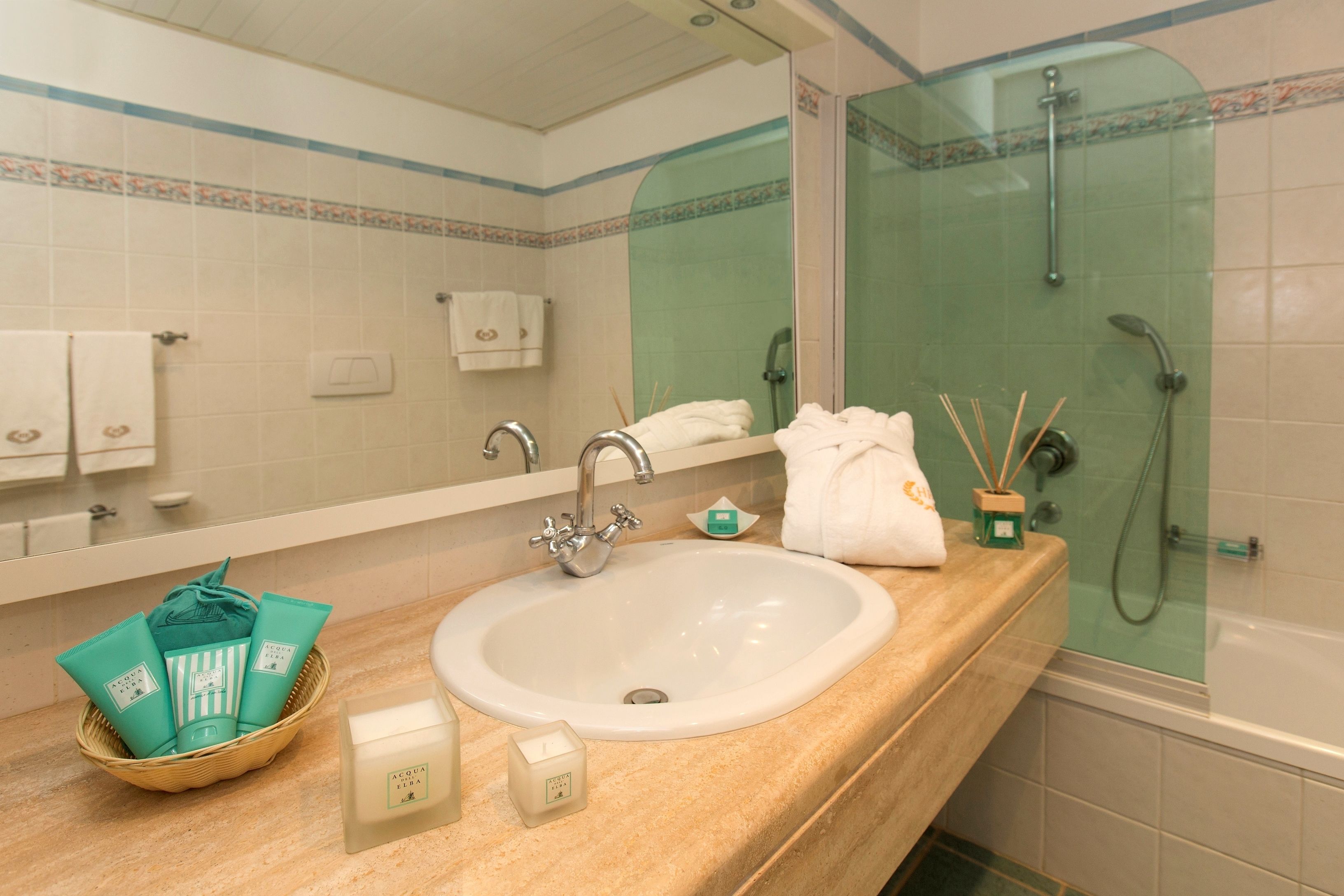 A bathroom with a sink, mirror, and shower. There are towels, toiletries, and a basket on the counter.