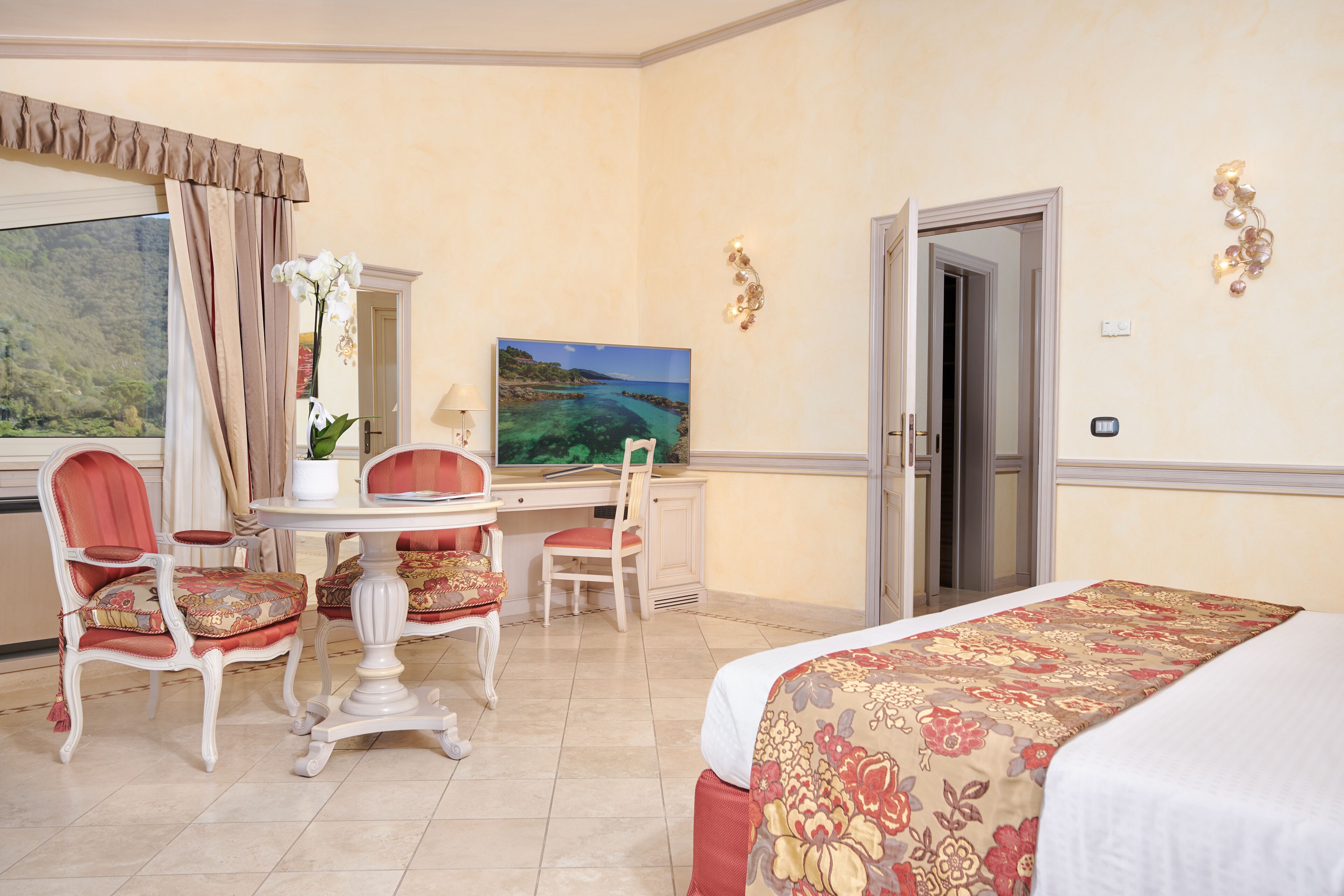 A hotel room with a bed, a desk with a chair, a television, and a window with curtains.