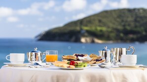 Desayuno con una mesa, cubiertos y un vaso de jugo de naranja con vistas panorámicas al mar.