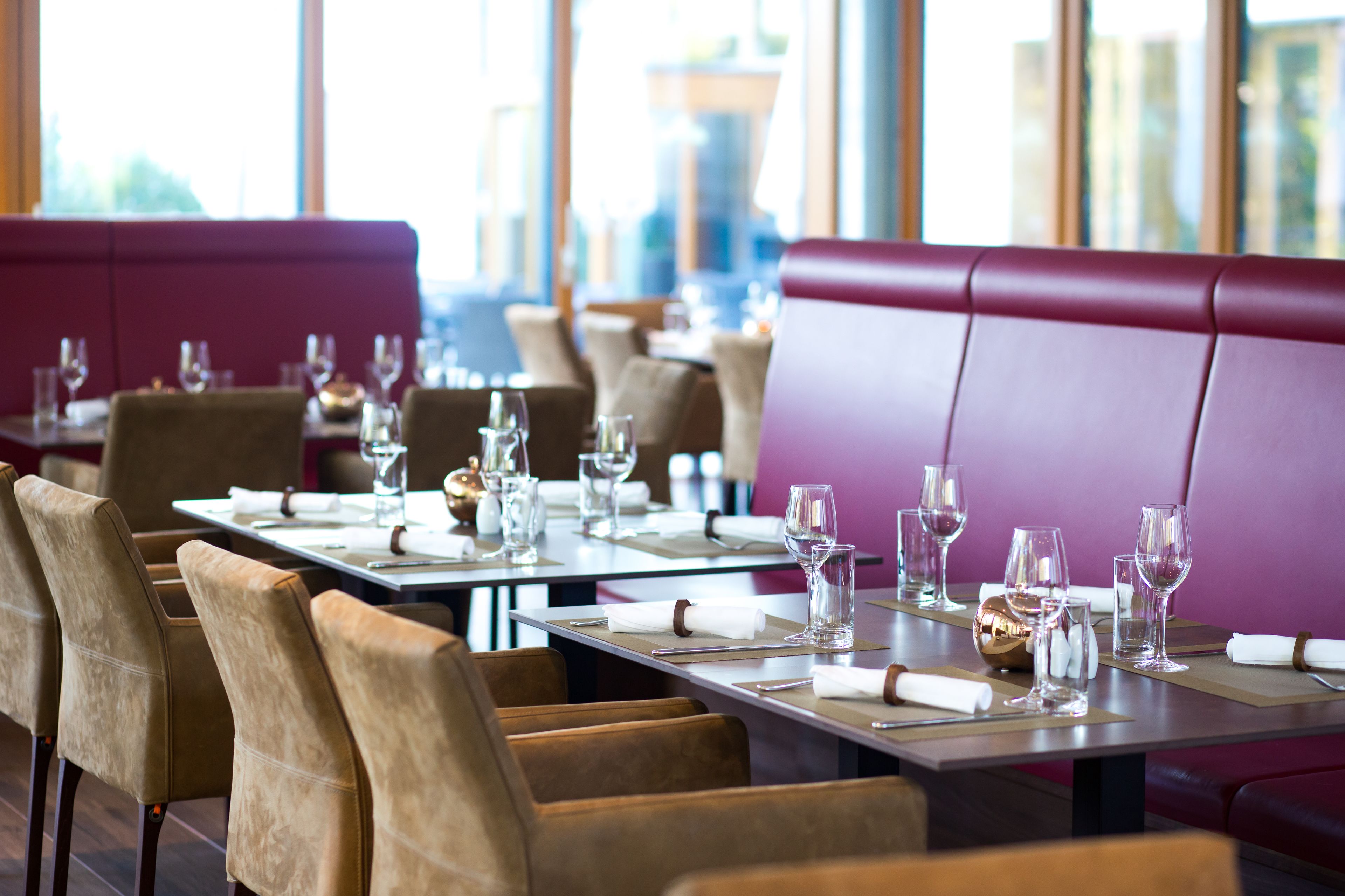 Un restaurant avec des tables dressées pour le service, doté de chaises confortables et d’un coin salon avec des banquettes violettes.