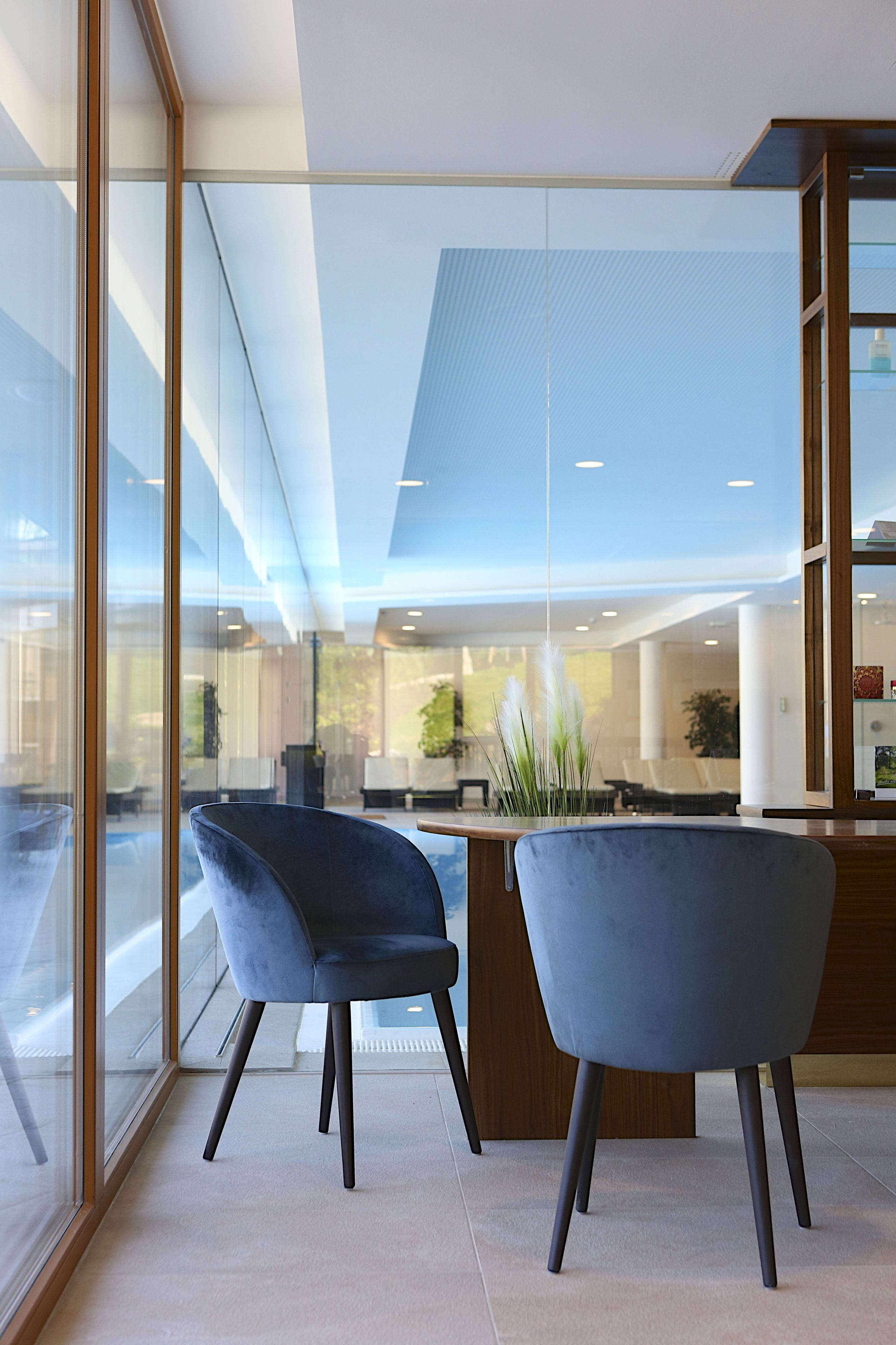 A modern office space with two dark blue chairs, a wooden reception desk, and large windows offering a view of the interior.