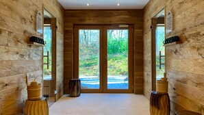 Un intérieur en bois avec une grande porte vitrée donnant sur l’extérieur, un banc en bois et une petite table avec une tasse.