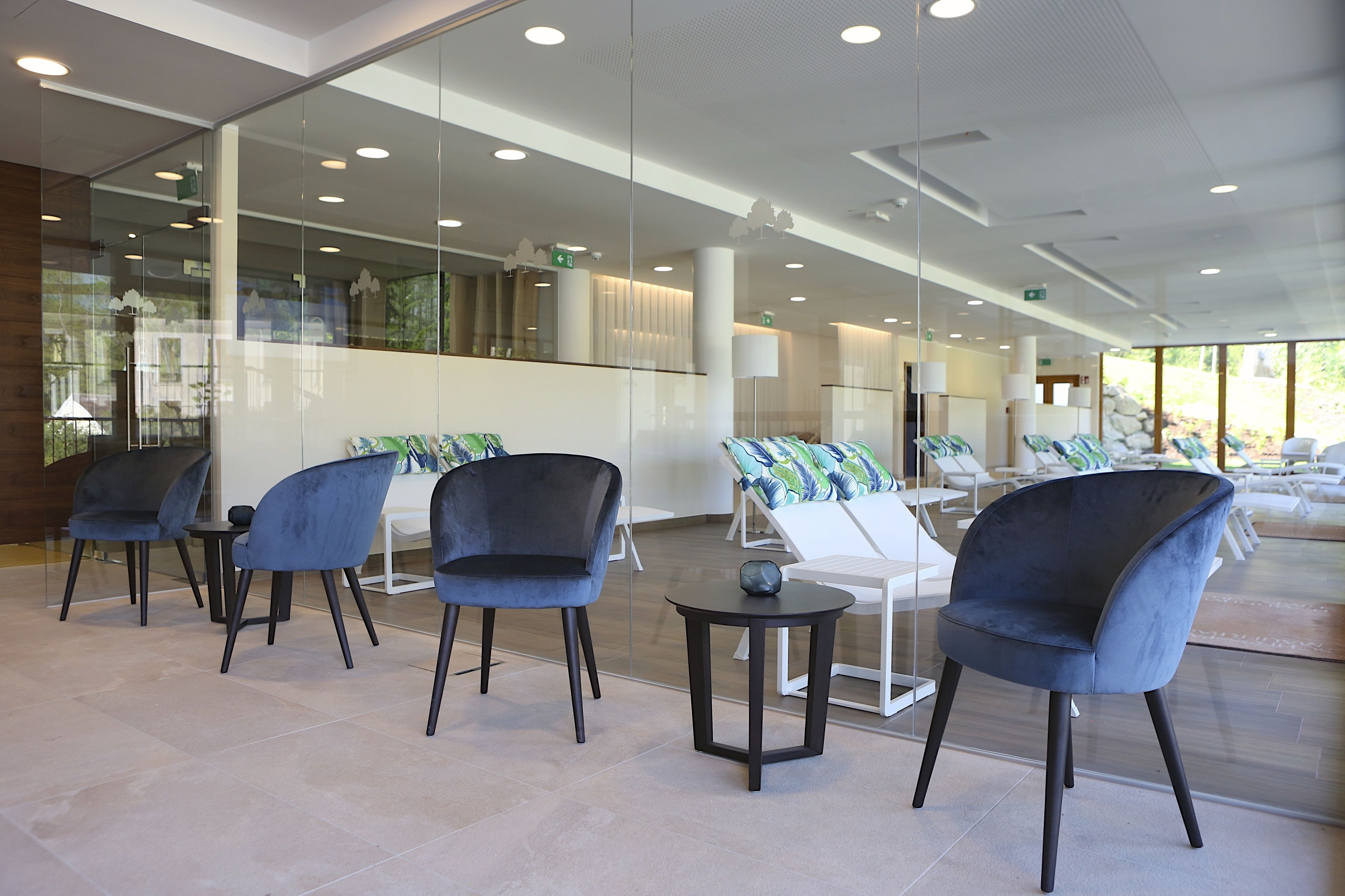 A modern indoor area with glass walls, several dark blue chairs, a white table, and a small round table with a decorative item.