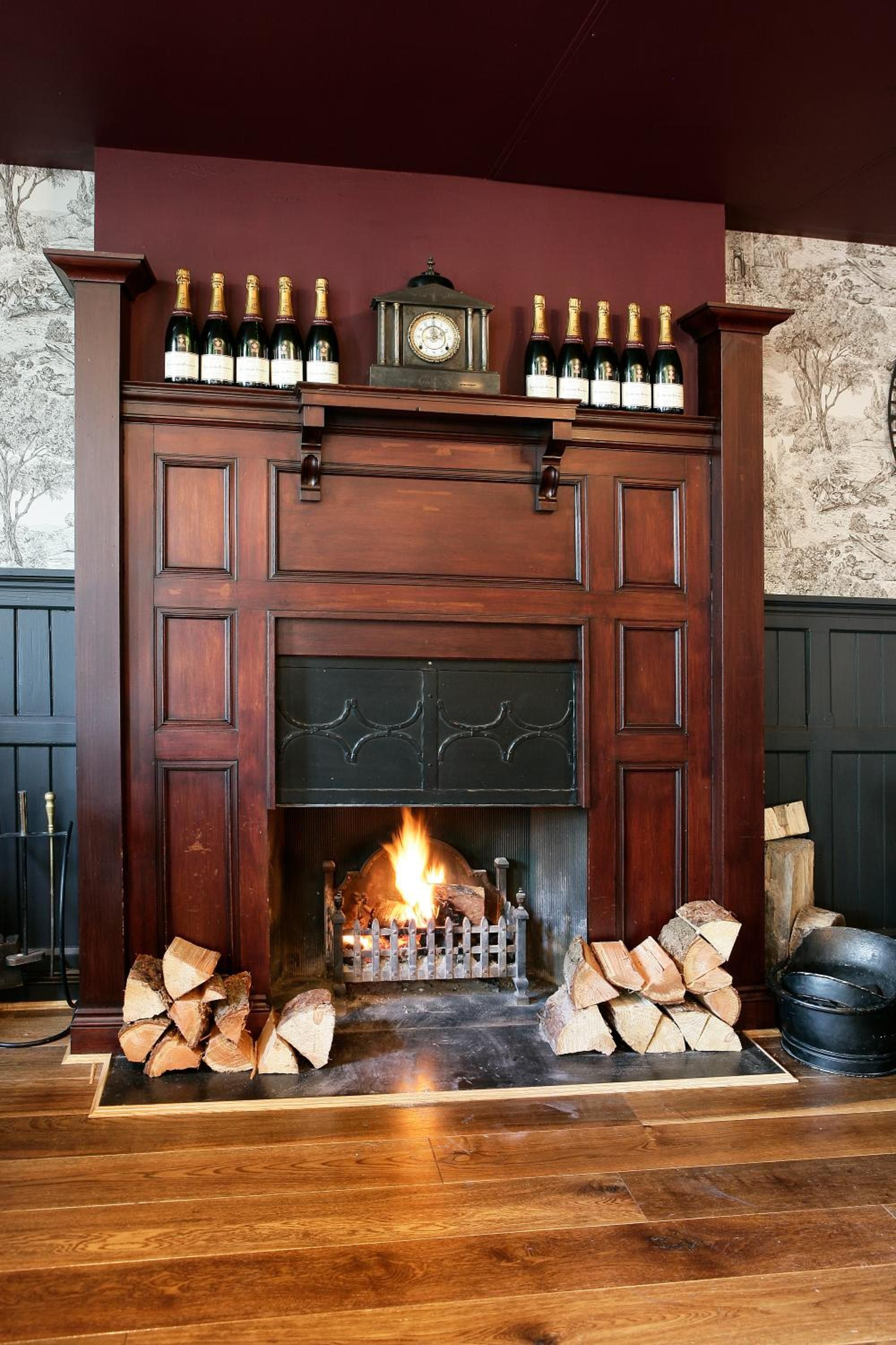 Una chimenea con repisa que muestra botellas, un reloj y leña.