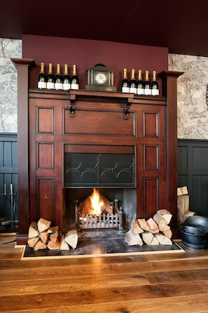 Una chimenea con repisa que muestra botellas, un reloj y leña.