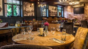 A restaurant with round tables set for dining, wooden walls, and a chandelier. - Alexander Pope (Twickenham)