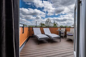 A wooden deck with two lounge chairs and a small table, overlooking a cloudy sky.