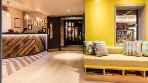 A reception area with a wooden reception desk, a sofa with patterned cushions, and a bookshelf. - Alexander Pope (Twickenham)