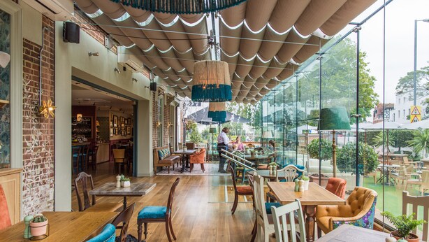 A spacious indoor dining area with wooden tables and chairs, a brick wall, and large windows offering a view of the outdoors. - Alexander Pope (Twickenham)