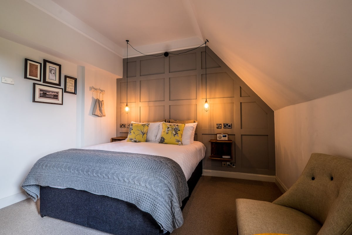 A bedroom with a bed, a chair, a nightstand, and a wall-mounted shelf.