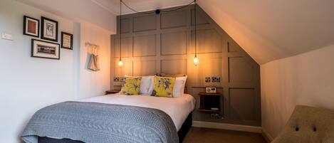 Een slaapkamer met een bed, een stoel, een nachtkastje en een wandplank.