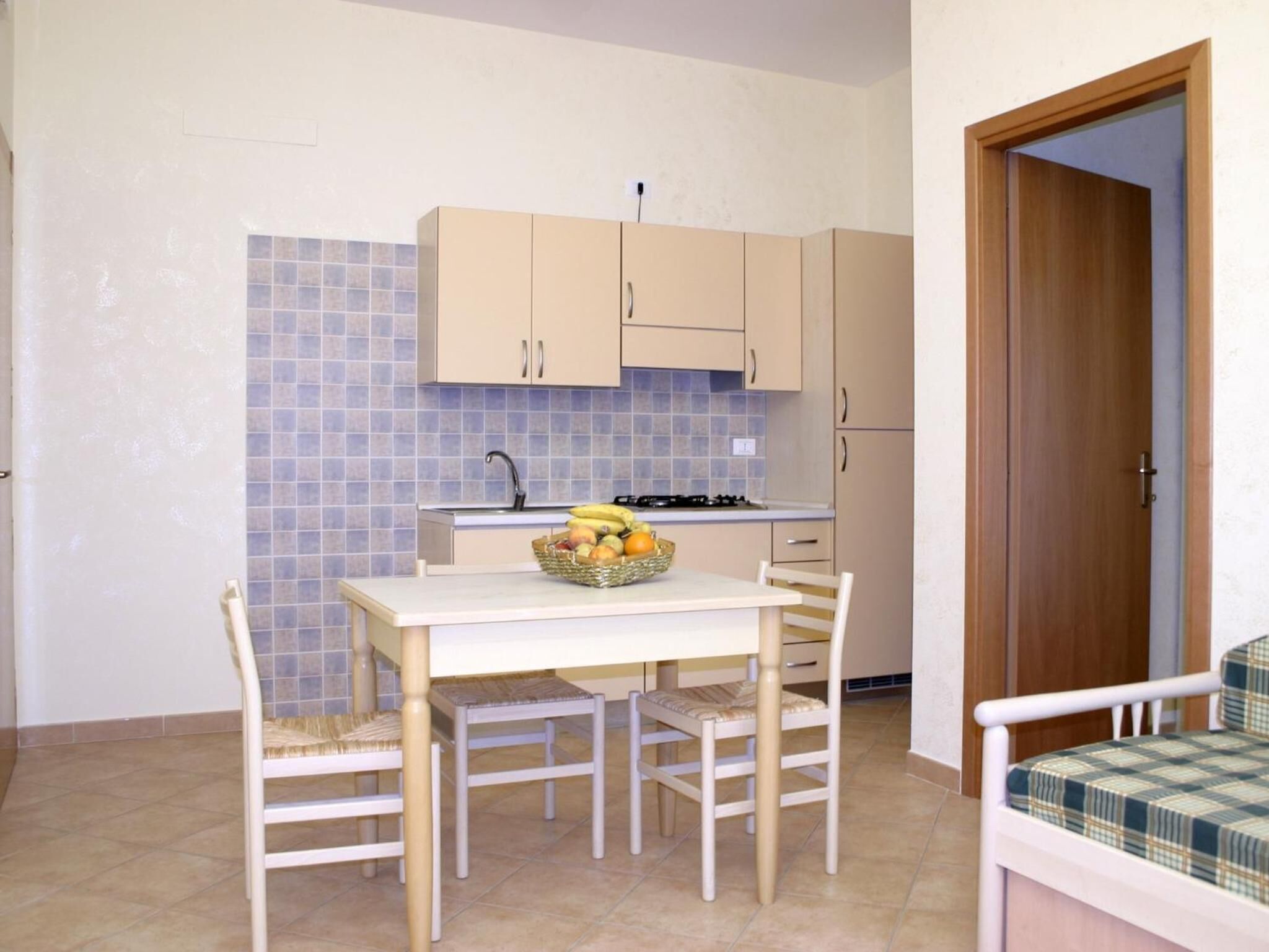 A compact kitchen with a dining table, chairs, a fruit basket, and a stove.