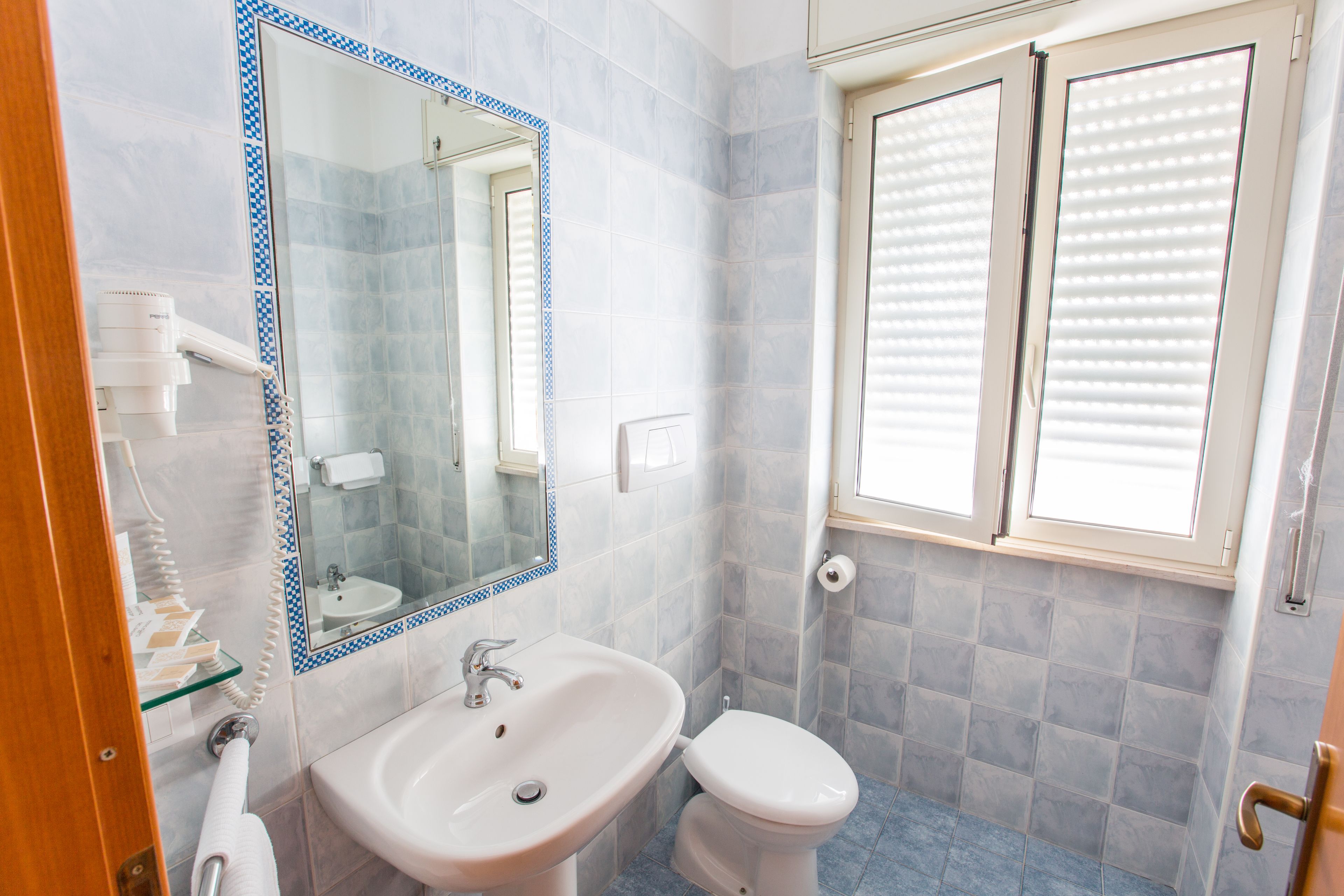A bathroom with a sink, mirror, toilet, and window with blinds.