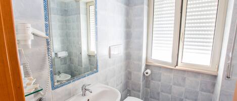A bathroom with a sink, mirror, toilet, and window with blinds.